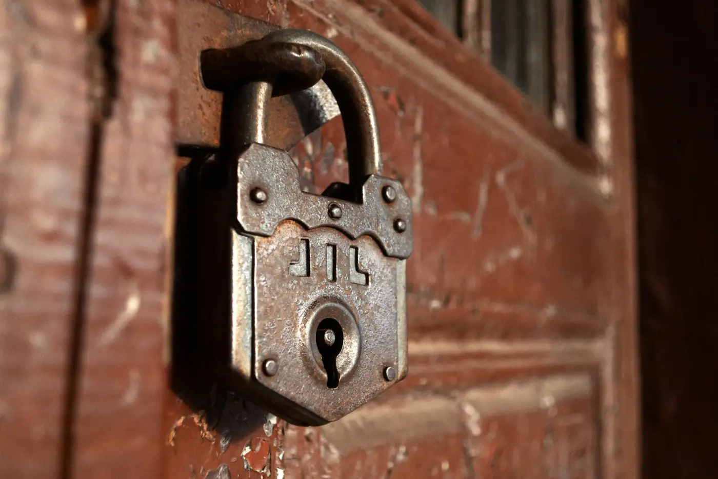 An old iron padlock hanging on a red-painted wooden door